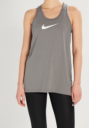 Osoba ubrana w szary bezrękawnik Nike i czarne legginsy, stojąca na jednolitym jasnym tle.