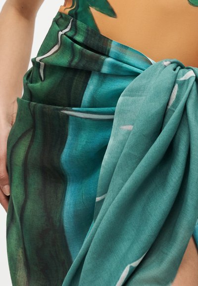 Gros plan d'un sarong noué avec des motifs de feuilles vertes et bleu sarcelle enroulé autour de la taille et de la hanche d'une personne.