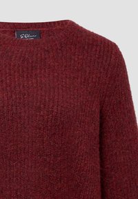 Zbliżenie na sweter o prążkowanym splocie w głębokim burgundzie z okrągłym dekoltem i widoczną czarną metką marki wewnątrz kołnierza.