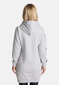 Hellgraues Hoodie-Kleid aus weichem Material, mit einer großen Kapuze, langen Ärmeln und gerippten Bündchen, versehen mit schwarzem Text entlang des Ärmels.