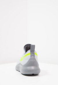 Gray Nike sneaker with neon yellow swoosh, pull tab on heel, and thick sole, shown from the back against a white background.