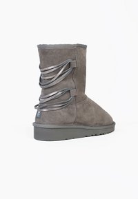 Stivale alla caviglia grigio in suede con punta rotonda, parte superiore in maglia e nastri decorativi argentati ai lati. Suola spessa e testurizzata per una buona aderenza.