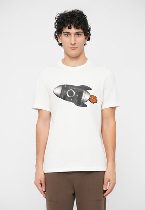 Young man with curly hair wearing a white t-shirt featuring a black and silver rocket graphic with orange flames.