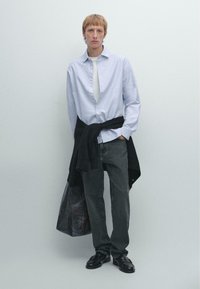 Camicia a maniche lunghe a righe azzurro chiaro, t-shirt bianca sotto, maglione nero legato in vita, jeans scuri, scarpe nere, borsa in tessuto morbido.