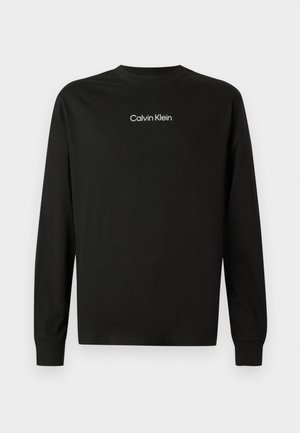Zwarte longsleeve crewneck shirt met het "Calvin Klein" logo in het wit gecentreerd op de borst, op een effen achtergrond.