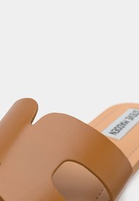 Sandale en cuir vegan couleur camel avec une bride large à découpe distinctive et une texture lisse, posée sur un fond clair.