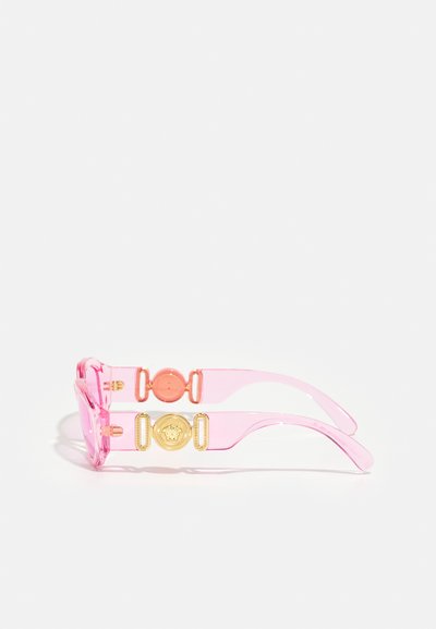Óculos de sol transparentes cor-de-rosa com lentes transparentes, apresentando detalhes em dourado e um logótipo redondo nos braços laterais.