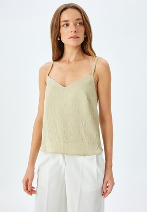Top de seda texturizada en verde salvia con tirantes ajustables y diseño de escote en V, combinado con pantalones blancos.