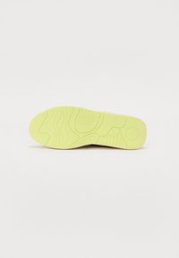 Shoe sole in bright yellow with a textured wave pattern and embossed brand name, featuring a round logo on the bottom edge.