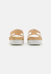 White sandals with natural woven accents, showcasing an open-back design and a thick white sole. Smooth texture, casual style.