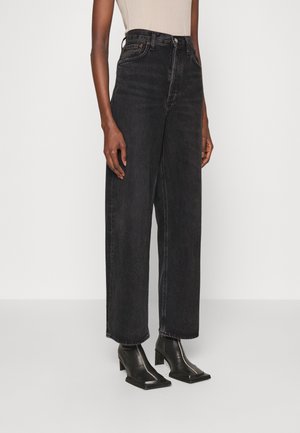 Jeans en denim noir taille haute avec une coupe évasée, comprenant cinq poches et une finition sombre légèrement texturée.