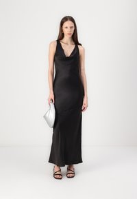 Black satin maxi dress with a cowl neckline and slim fit, paired with a silver clutch and black strappy sandals. Smooth texture, elegant design.