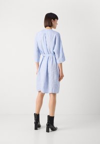 Svetlo modra lanena obleka s tremi četrtinami rokavi, z pasom, ki je na hrbtni strani nagubana. Ujemajoč se z črnimi gležnjerniki s širokim peto.