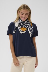 Jūras spēku zila kokvilnas t-kreklā ar brīvu piegriezumu, ko papildina rakstainā zīda šalle ar režģa līnijām un dzelteniem akcentiem.