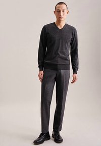 Grå V-hals sweater og matchende skræddersyede bukser i tekstureret stof. Simpelt design med en tætsiddende silhuet, kombineret med sorte sko.