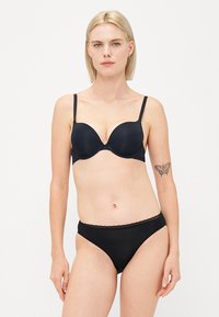 Reggiseno imbottito nero con spalline regolabili e texture liscia, abbinato a mutandine nere con bordi di pizzo, entrambi progettati per comfort e vestibilità.
