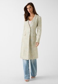 Licht gestructureerd, pastelkleurig blazer met een aansluitende pasvorm, enkele knoopsluiting en twee voorzakken, gecombineerd met wijde jeans.