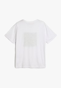 Camiseta de algodón blanca de manga corta, con cuello redondo y un sutil detalle de textura cuadrada en la parte posterior. Corte holgado, textura suave.