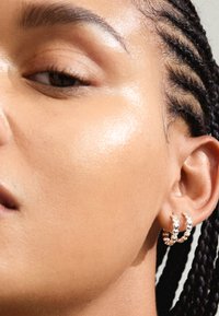 Orecchini a cerchio in argento con design intrecciato, caratterizzati da sezioni alternate lucide e testurizzate, mostrati in primo piano su un orecchio di un modello.