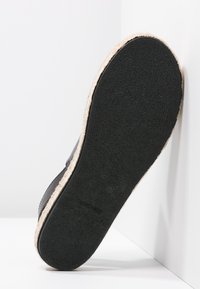 Černá podrážka tenisky s texturovaným povrchem a okrajem středové části v světle hnědé textilii. Obsahuje hladký materiál a zakřivený design paty.