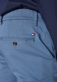 Pantaloni corti azzurro chiaro con un tessuto texturizzato, dotati di una tasca posteriore con un bottone scuro e un piccolo logo a tre colori.