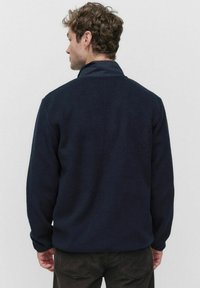 Granatowy polarowy sweter z miękką teksturą, stojącym kołnierzem i długimi rękawami. Charakteryzuje się luźnym krojem i minimalistycznym designem.