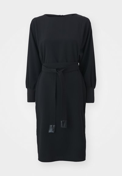 Vestido preto feito de tecido suave, com decote redondo, mangas longas e uma cintura com cinto. O cinto tem detalhes pretos brilhantes.