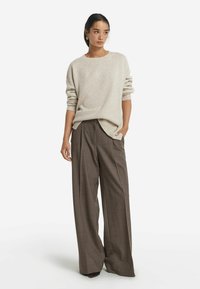 Beige Strickpullover mit rundem Ausschnitt, kombiniert mit weit geschnittenen braunen Karohosen. Der Stoff wirkt weich, hat eine sichtbare Textur und fällt locker.
