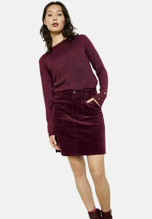 Bordeauxkleurige trui met lange mouwen en knoopaccenten, gecombineerd met een bijpassende corduroy rok met zijzakken en een getailleerde silhouet.