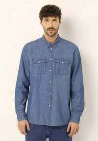 Camicia in denim azzurro chiaro, con due tasche sul petto, chiusura a bottoni e maniche lunghe con polsini abbottonati, tessuto liscio.