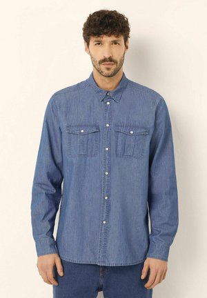 Denim shirt in light blue, featuring two chest pockets, button closure, and long sleeves with buttoned cuffs, smooth texture.