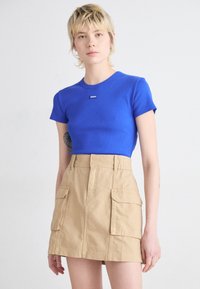 T-shirt blu a righe con patch nero, abbinato a una gonna cargo beige a vita alta con tasche laterali e un design strutturato.