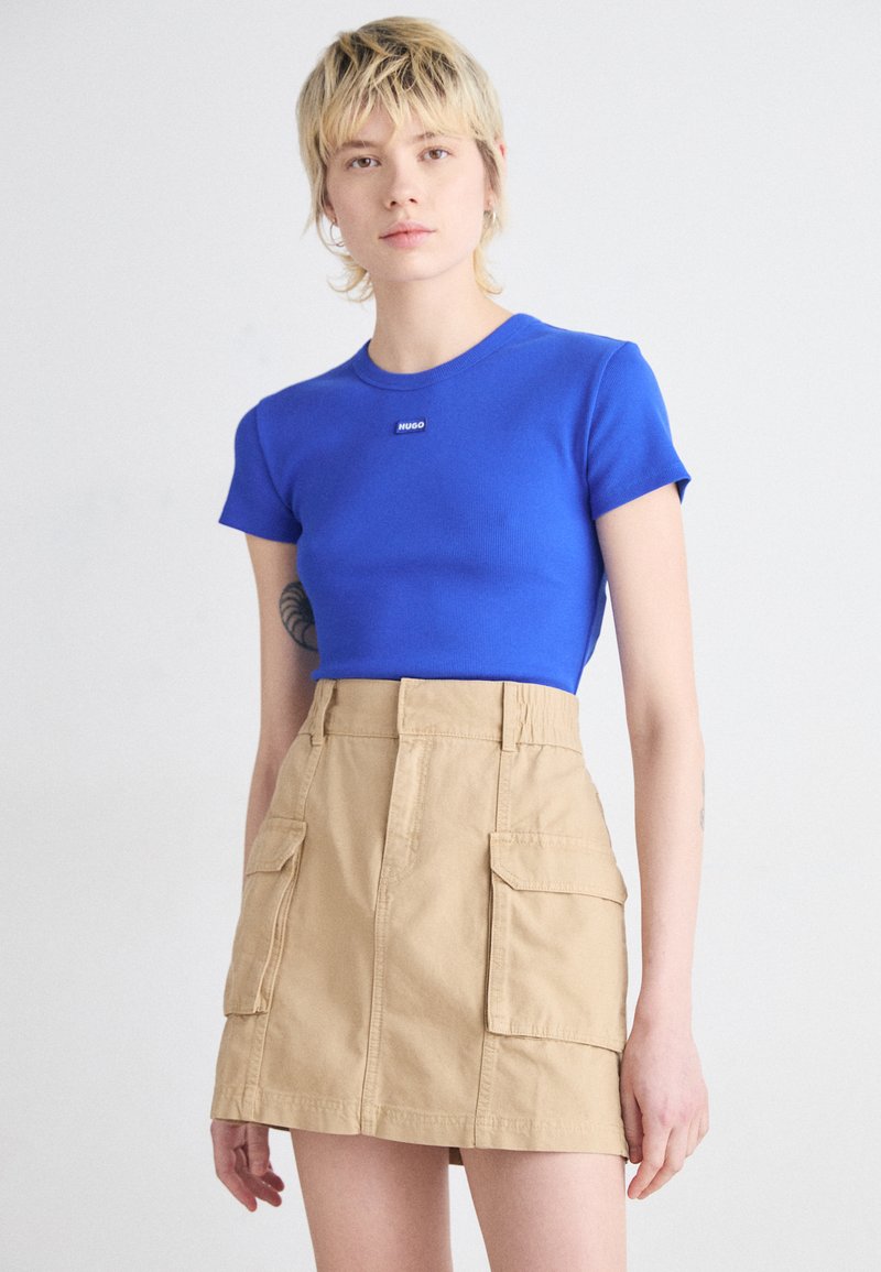 T-shirt blu a righe con patch nero, abbinato a una gonna cargo beige a vita alta con tasche laterali e un design strutturato.