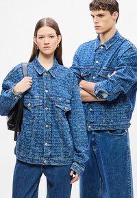 Denim jakne svijetloplave boje s uzorkom cijelog teksta, prednjim džepovima i kopčama na pritisak; uparene s odgovarajućim traper hlačama.