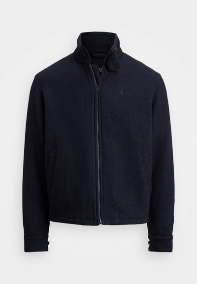 Giacca in misto lana navy con zip, collo alto e due tasche laterali. Tessuto testurizzato con un sottile motivo a spina di pesce.