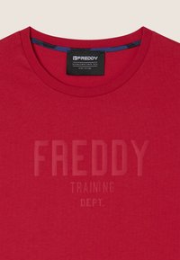 Camiseta roja de cuello redondo con el texto "FREDDY TRAINING DEPT." impreso en la parte frontal y una etiqueta de marca "Freddy" negra dentro del cuello.