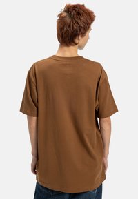 Brązowy, oversize bawełniany t-shirt z krótkimi rękawami i okrągłym dekoltem. Posiada prosty design bez wzorów i widocznych elementów.