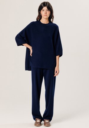 Marineblauwe oversized sweater met korte mouwen, gecombineerd met wijde broek in dezelfde kleur. Glad stofoppervlak, minimalistisch design.