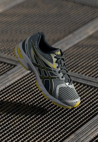 Gray running shoe with mesh upper, yellow accents, black laces, and a textured sole. Lightweight design suitable for athletic use.