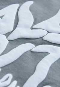 Harmaa kangas, jossa on tekstuurinen valkoinen abstrakti kuvio. Pintojen näyttää olevan pehmeä, ja kohotetuilla alueilla on sileät muodot ja orgaanisia muotoja.