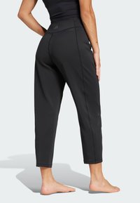 Čierne športové nohavice s priliehavým pásom, skrátenou dĺžkou, hladkou textúrou a viditeľným šitím pozdĺž bokov. Jednoduchý, funkčný dizajn.