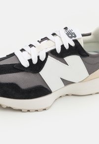 Sneaker med ett grått mesh-ovandel, svarta mockadetaljer, vit läderlogotyp och vita snören. Texturerad sula och kontrasterande material.