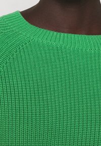 Grüner Strickpullover mit rundem Ausschnitt. Texturiertes Muster und gerippte Details am Kragen. Weicher, lebendiger Stoff.