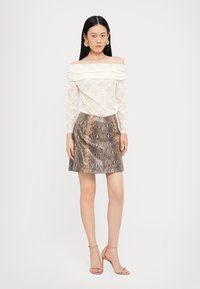 Off-shoulder hvit bluse i blonder med teksturdetaljer; brun faux skinn mini skjørt med slangeskinnsmønster; nude stroppede hæler.