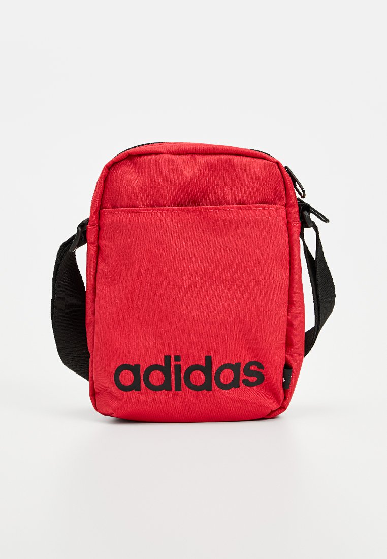 Bolso de tela rojo bandolera con una cremallera negra, una correa ajustable y un destacado logo negro de Adidas en la parte frontal. Diseño rectangular simple.