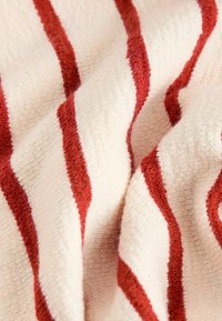 Cotton fabric in cream with bold, textured red stripes. The material features a soft, plush texture, creating a cozy appearance.