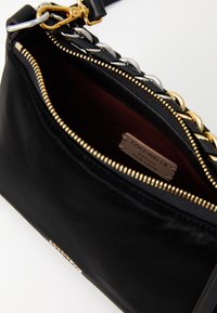 Borsa in pelle nera con zip dorata e dettagli in catena, parzialmente aperta per mostrare l'interno bordeaux e l'etichetta "Coccinelle Autentica Pelle Italiana".