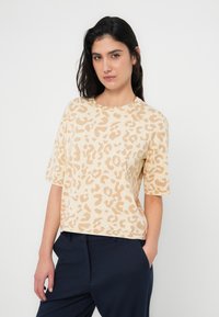 Μπλούζα μπεζ με κοντά μανίκια και σχέδιο λεοπάρ, άνετη εφαρμογή, πλεκτή υφή και ριμπ λαιμόκοψη, σε συνδυασμό με σκούρο παντελόνι.