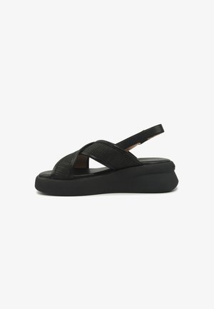 Crna sandala na klin s križno isprepletenim teksturiranim remenčićima i podesivim remenom na stražnjoj strani na bijeloj pozadini.