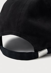 Black cotton baseball cap with a curved brim, stitched detailing, and an adjustable strap. Features a metallic branding accent on the strap.